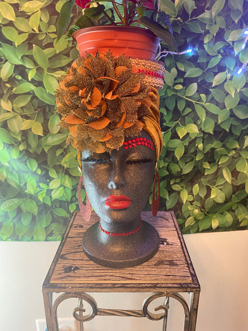 Decorative head with floral design on a stand against a green leafy background