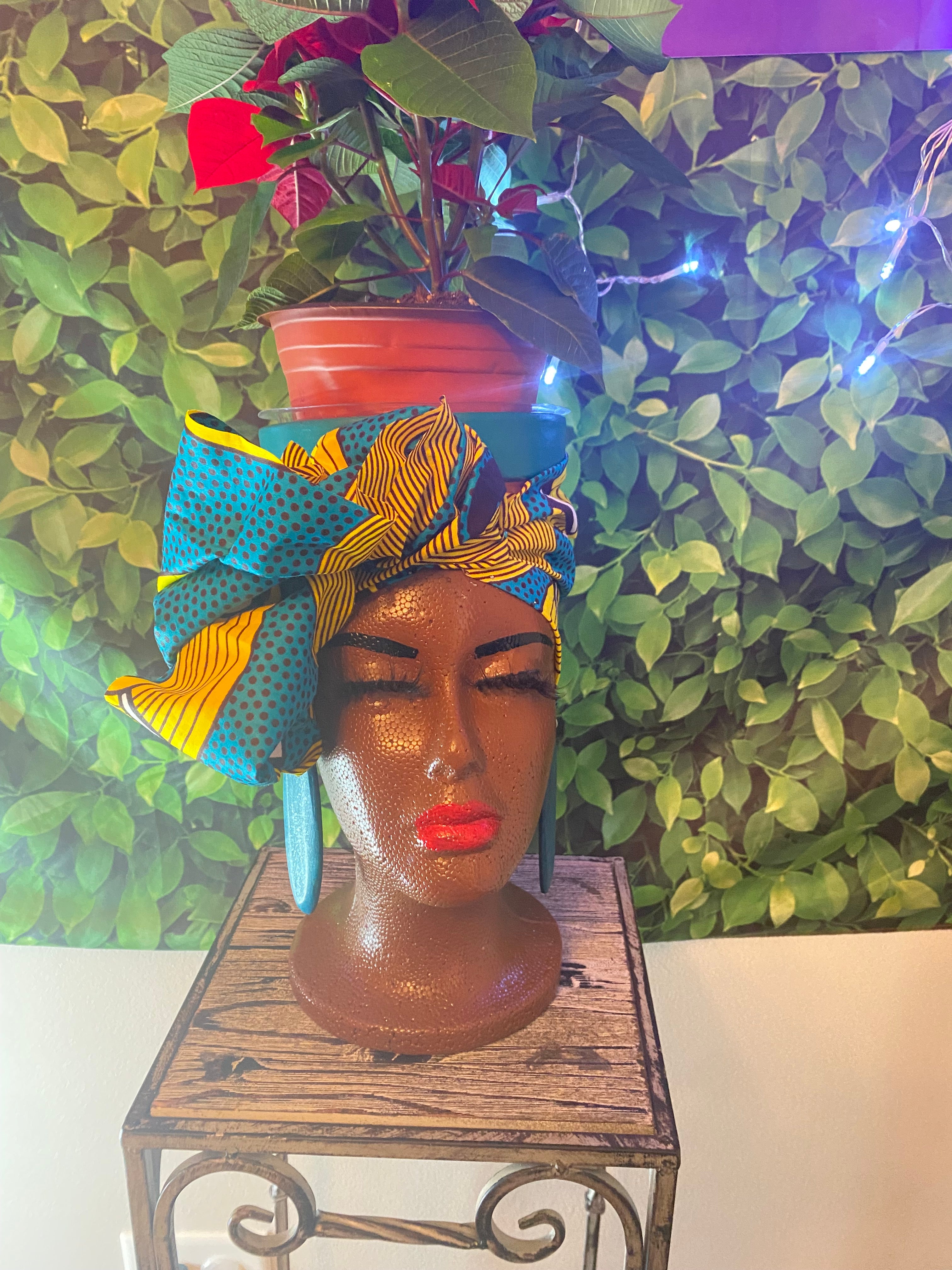 Decorative head with colorful fabric and red lipstick against a green leafy background
